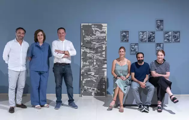 Seis miembros del jurado posan frente a pared azul junto a las obras ganadoras del XXVII Certamen Gregorio Prieto.