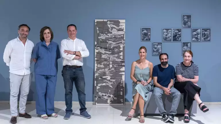 Seis miembros del jurado posan frente a pared azul junto a las obras ganadoras del XXVII Certamen Gregorio Prieto.