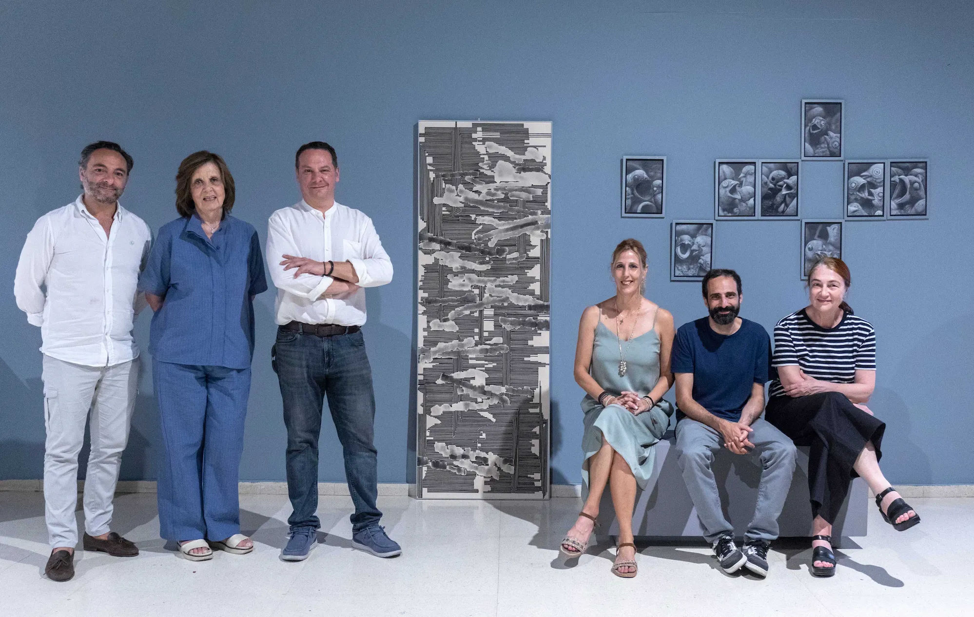 Seis miembros del jurado posan frente a pared azul junto a las obras ganadoras del XXVII Certamen Gregorio Prieto.