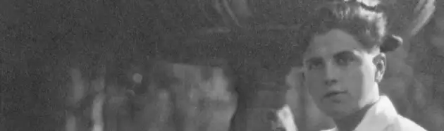 Retrato parcial de Gregorio Prieto en el Parque del Retiro, Madrid (1918–1919). La imagen en blanco y negro muestra un encuadre panorámico centrado en el rostro y busto de un joven Gregorio Prieto. Su expresión es seria y fija la mirada fuera del encuadre, hacia el espectador. Lleva una camisa clara abotonada hasta el cuello, sin chaqueta, y su cabello está cuidadosamente peinado hacia atrás con volumen. El fondo es difuso y está dominado por una gran fuente de piedra ornamentada, que se eleva justo detrás de él, parcialmente desenfocada, indicando que la escena transcurre al aire libre. La iluminación es tenue y natural, posiblemente capturada a la sombra de los árboles del Parque del Retiro en Madrid. El estilo de la fotografía, la ropa del retratado y la calidad de la imagen remiten a principios del siglo XX. Esta imagen corresponde a un fragmento de una fotografía más amplia realizada entre 1918 y 1919.